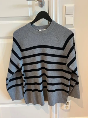 Grå stickad tröja med svarta ränder - Snygg grå stickad tröja med svarta horisontella ränder. Tröjan har rund halsringning, vida ärmar och en avslappnad passform. Perfekt för dig som gillar enkel men trendig stil. Materialet känns mjukt och bekvämt.