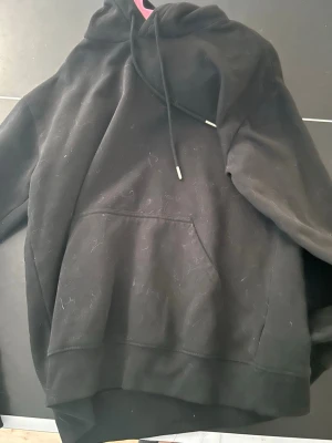 Svart hoodie med magficka - En klassisk svart hoodie med huva och dragsko samt en stor magficka framtill. Hoodien har ribbade muddar vid ärmslut och nederkant. Perfekt för en avslappnad och stilren look. Är lite hårig på bilden men de kan jag rulla bort 