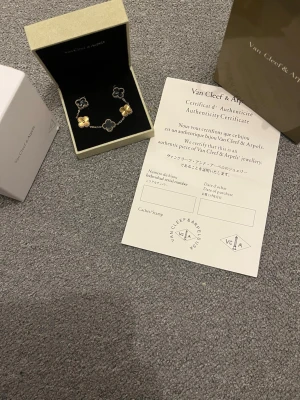 Van Cleef & Arpels Alhambra armband - Exklusivt armband från Van Cleef & Arpels Alhambra-kollektion. Armbandet har ikoniska fyrklöverformade hängen i guld och svart, länkad med en tunn kedja. Levereras med originalask, påse och äkthetsintyg. Perfekt för dig som gillar lyxiga accessoarer. Du får en dior armband på köpet