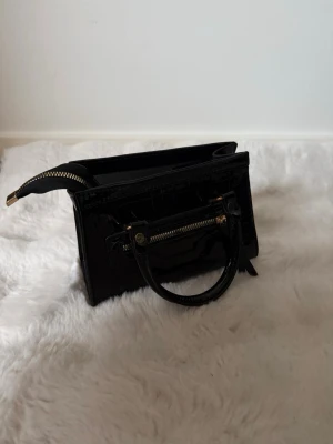 Glansig svart handväska med gulddetaljer  - Jag har aldrig använt den då den inte passade mig 