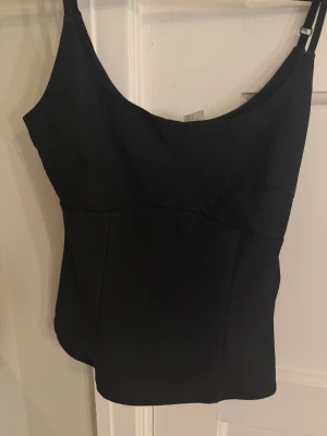 Svart korsettliknande linne med smala axelband - Snygg svart linnetopp med smala, justerbara axelband och enkel, stilren design. Toppen har en lätt figurnära passform och är perfekt att matcha med jeans eller kjol. Från h&m i s