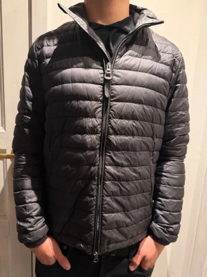Woolrich jacka  - Snygg svart  dunjacka från Woolrich med horisontella sömmar och hög krage. Jackan har hel dragkedja framtill och två sidofickor med dragkedja. Perfekt för kalla vinterdagar och enkel att matcha med olika outfits.