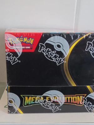 Pokémon Mega Evolution boosterbox - Säljer en Pokémon Mega Evolution boosterbox från Pokémon Trading Card Game. Boxen är svart med färgglada detaljer och innehåller samlarkort. Perfekt för dig som vill bygga din samling eller spela med vänner.