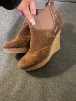 Bruna kilklackade stövletter Diesel - Snygga bruna stövletter från Diesel med kilklack och ovandel i mocka. Skorna har elastiska partier på sidorna för enkel påtagning och en markerad söm längs ovandelen. Perfekta för dig som vill ha både höjd och komfort. Äkta läder!OBS! Säljer alla klackar på min plick åt min mamma.