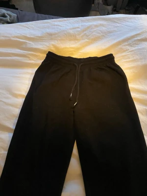 Svarta mjukisbyxor med dragsko - Säljer ett par svarta mjukisbyxor med elastisk midja och dragsko. Byxorna har en klassisk rak passform och är perfekta för chill dagar. Materialet känns mjukt och bekvämt. Jag som är 177cm lång sitter som super bra i längden.
