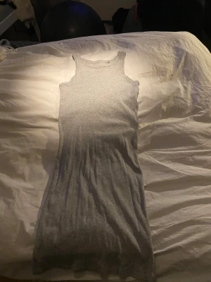 Grå ribbad långklänning - En enkel och stilren grå långklänning i ribbad bomull. Klänningen är ärmlös med breda axelband och har en rak, kroppsnära passform. 