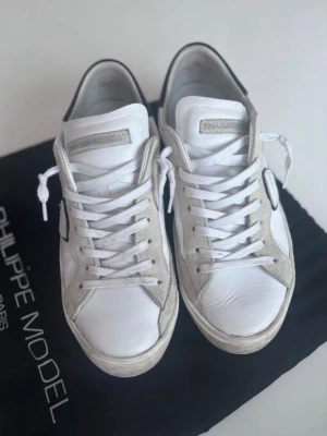 Philippe model, strl 41, superbra skick!!! - Snygga vita sneakers från Philippe Model med detaljer i grå mocka och svart häl. Klassisk låg modell med vita skosnören och diskret logga på sidan. Ovandelen är i läder och mocka vilket ger en stilren och trendig look.