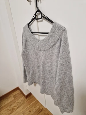 Grå stickad tröja med bred krage - Mysig grå stickad tröja med bred ribbad krage och långa ärmar. Tröjan har en avslappnad passform och ribbade muddar vid ärmslut och nederkant. Perfekt för kyliga dagar och enkel att matcha med olika outfits.