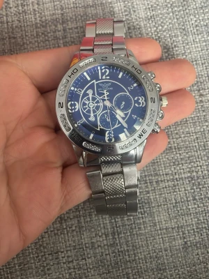 Silverfärgad Excellanc herrklocka - Stilren herrklocka från Excellanc med blå urtavla och silverfärgat armband i metall. Klockan har flera dekorativa urtavlor, tydliga siffror och detaljerade visare. Perfekt accessoar för dig som gillar en sportig och modern look.