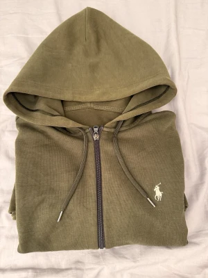 Polo Ralph Lauren Zip Hoodie – Grön – Original - En clean staple med premiumkänsla.  Zip hoodie från Polo Ralph Lauren i olive/grön ton med diskret broderad logga på bröstet. En tidlös hoodie som funkar perfekt året runt – lätt att styla och alltid rätt.  • 100% original Polo Ralph Lauren   • Storlek: S   • Färg: Olive / grön   • Skick: Bra   • tag saknas därav pris   Mjuk och bekväm kvalitet med klassisk passform. Perfekt för vardag, lager-på-lager eller casual outfits.  Skickas snabbt 🚚   Kolla gärna min prof