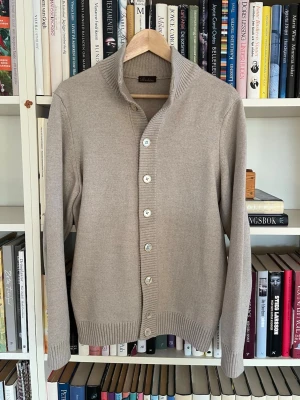 Beige kofta från Stenströms - Snygg beige helt ny kofta från Stenströms med ribbad krage och knäppning framtill. Tillverkad i mjukt material och har långa ärmar samt ribbade muddar vid ärmslut och nederkant. Perfekt för lager-på-lager och stilrena outfits.