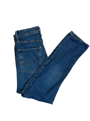Blå raka jeans från Jack&Jones - Klassiska blå jeans från Jack and Jones med rak passform och fem fickor. Jeansen har normal midja och är tillverkade i slitstark denim. Perfekta för en avslappnad och tidlös stil.