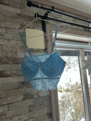 Ljusblå spets-bh med detaljer - Snygg ljusblå bh i spets med vadderade kupor och dekorativa band över bysten. Bh:n har justerbara axelband och längre spetskant nedtill för en trendig look. 