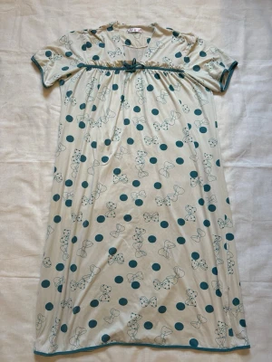 Beige nattlinne med rosett- och prickmönster - Sött nattlinne från Lindex i beige med gröna prickar och rosetter. Kort ärm, v-ringning och dekorativ rosett under bysten. Mjukt och följsamt material, perfekt för mysiga kvällar hemma.