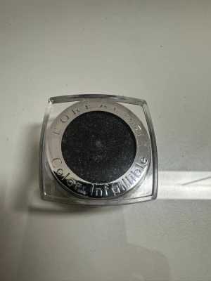 L'Oréal Color Infaillible svart Loose eyeshadow - Snygg svart Loose eyeshadow från L'Oréal Paris Color Infaillible-serien. Skuggan har en intensiv svart färg med skimrande glittereffekt och kommer i en rund dosa med genomskinligt lock och silverdetaljer. Perfekt för att skapa dramatiska ögonmakeuper.