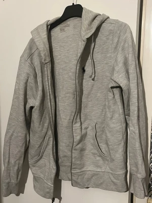 Grå hoodie från Polo Ralph Lauren - Snygg grå hoodie från Polo Ralph Lauren med dragkedja, två fickor framtill och klassisk huva med dragsko. Tillverkad i mjukt material och har den ikoniska lilla loggan broderad på bröstet. Perfekt för en chill och stilren look. Storlek s men passar xs