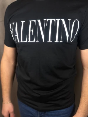 Svart Valentino t-shirt med tryck - Svart t-shirt från Valentino med stort vitt logotryck över bröstet. Klassisk passform och rund halsringning, perfekt för en stilren och trendig look. Tillverkad i mjuk bomull som känns skön mot huden.