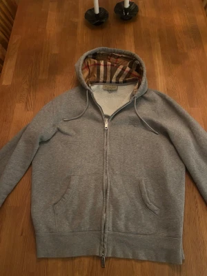  Burberry zip - Snygg grå hoodie från Burberry med dragkedja och klassisk stil. Perfekt för dig som gillar stilrena plagg med exklusiv känsla. Materialet är mjukt och bekvämt, perfekt för chill dagar. Nypris 9000-10000! Såklart äkta…                                           Mvh