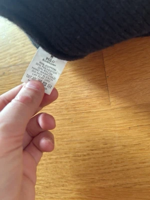 Svart ribbstickad mössa Polo Ralph Lauren - Klassisk svart ribbstickad mössa från Polo Ralph Lauren. Tillverkad i en mjuk blandning av bomull, polyester och nylon. Mössan har vikt kant och enkel, stilren design som passar till det mesta.