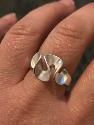 Ring vågig ring i modern design - Unik ring i silverfärgat material med vågig, abstrakt form. Ringen har en matt finish och är öppen i designen vilket ger en cool och modern känsla. Perfekt för dig som gillar statement-smycken och vill sticka ut med din stil.