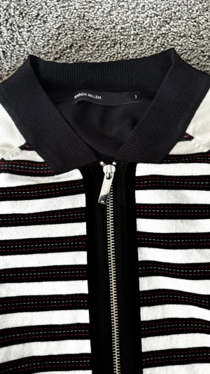 Randig cardiganjacka från Karen Millen - Snygg cardiganjacka från Karen Millen med svartvitt randigt mönster och diskreta röda detaljer. Jackan har dragkedja framtill, svarta muddar och krage samt lång ärm med randigt avslut. Materialet känns mjukt och stretchigt, perfekt för en trendig look.