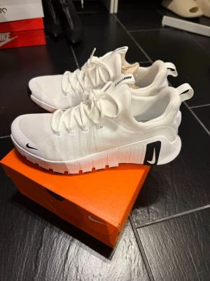 Vita Nike Free Metacon sneakers - Snygga vita Nike Free sneakers med låg profil och svart swoosh på sidan. Ovandelen är i mesh för bra andningsförmåga och skon har en flexibel sula i gummi för skön komfort. Perfekta för dig som gillar stilrena och sportiga sneakers.