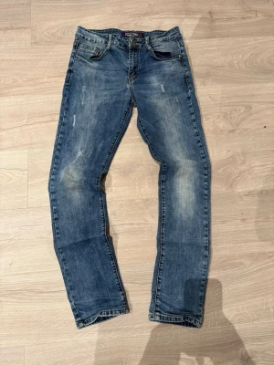 Yiman jeans - Säljer ett par blå jeans med raka ben och slitna detaljer på både fram- och baksida. Jeansen har klassisk femficksdesign och ljusare partier för en cool, använd look. Perfekta för dig som gillar en avslappnad stil.