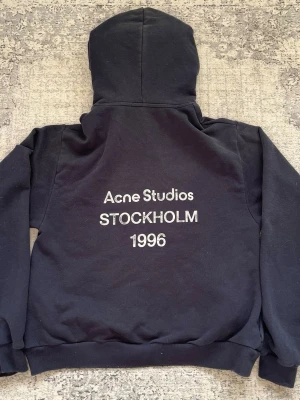 Svart hoodie Acne Studios Stockholm - Svart hoodie från Acne Studios med vit text på ryggen där det står 'Acne Studios STOCKHOLM 1996'. Klassisk passform med huva och ribbade muddar. Perfekt för dig som gillar streetwear och vill ha en stilren look med en touch av Stockholm Såklart finns det kontoutdrag osv skriv och fråga bara!!❤️❤️.
