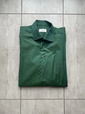 Grön skjorta från Eton - Snygg grön skjorta från Eton med klassisk krage och knäppning framtill. Skjortan har lång ärm med manschett och är tillverkad i ett slätt bomullstyg. Perfekt för dig som vill ha en stilren och tidlös look. Nypris -:1700. Vid frågor eller funderingar skriv gärna!