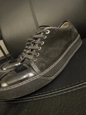 Svarta sneakers i mocka och lack - Snygga svarta sneakers med ovandel i mocka och tåparti i glansigt lackmaterial. Skorna har svarta skosnören, diskreta sömmar och en svart sula. Insidan är beige och ger en schysst kontrast. Perfekta för dig som gillar stilrena detaljer. Uk8