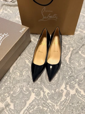 Svarta lackpumps från Christian Louboutin - Snygga svarta pumps i lack från Christian Louboutin med klassisk spetsig tå och hög klack. Skorna har den ikoniska röda sulan och elegant siluett, perfekta för att lyfta vilken outfit som helst.