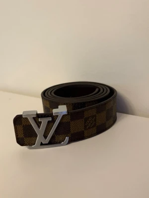 Brunt bälte - Stilrent brunt bälte med silver logga i gott skick 120cm