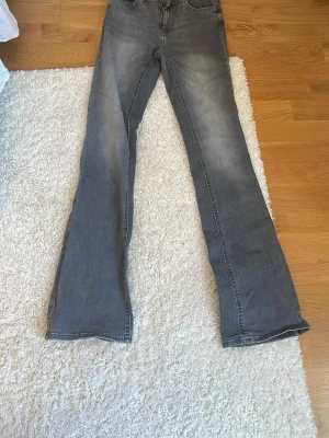 Grå bootcut jeans med utsvängda ben - Snygga grå jeans med bootcut-modell och utsvängda ben. Jeansen har klassisk femficksdesign och subtila slitningar framtill för en cool look. Perfekta för dig som gillar retrostil och vill ha ett par jeans som sticker ut.