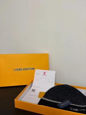 Mörkgrå mössa - Snygg mörkgrå mössa med diskret monogrammönster och vit logotypbrodyr framtill. Mössan har en klassisk form och är tillverkad i mjukt material som känns lyxigt. Perfekt accessoar för dig som vill ha något exklusivt och stilrent.