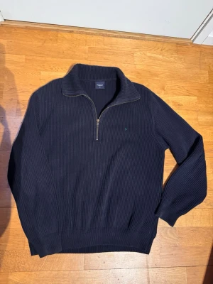 Mörkblå stickad tröja Boomerang - Mörkblå stickad tröja från Boomerang med halv dragkedja och hög krage. Tröjan har ribbstickad struktur, långa ärmar och diskret logga på bröstet. Perfekt för lager på lager och en stilren look. Lite tjockare material 