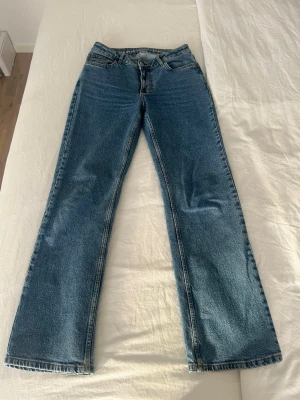 Blå raka jeans med medelhög midja - Klassiska blå jeans med rak passform och midrise hög midja. Jeansen har fem fickor och stängs med dragkedja och knapp. Perfekta för en avslappnad och trendig look. Materialet är kraftig denim i bomull.