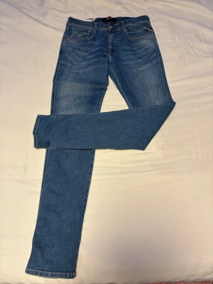 Blå slim fit jeans från replay - Snygga blå jeans från replay i modellen slim fit anbass. Jeansen har klassisk femficksdesign, normal midja och raka ben. Tillverkade i ett stretchigt material för extra komfort. Perfekta för en trendig och avslappnad stil. Tyvärr en lite skada som synd på bild bortsett från den så perfekt i condition.