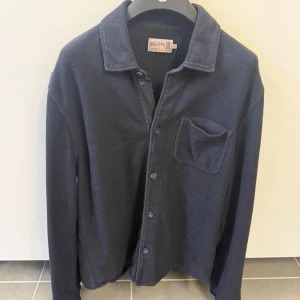 Mörkblå skjorta från Morris - Stilren mörkblå skjorta från Mards med klassisk krage och bröstficka. Skjortan har långa ärmar och knäppning framtill. Perfekt för en avslappnad men snygg look. Tillverkad i mjukt bomullsmaterial.