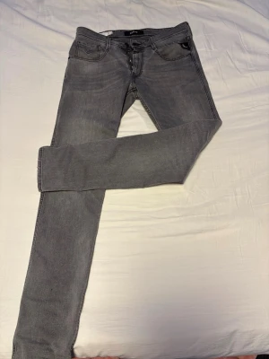 Grå slim fit jeans från Replay - Säljer ett par grå slim fit jeans från Replay, modell Anbass. Jeansen har klassisk femficksdesign, dragkedjegylf och smal passform. Perfekta för dig som gillar en modern och stilren look. Materialet är mjukt och stretchigt för extra komfort.