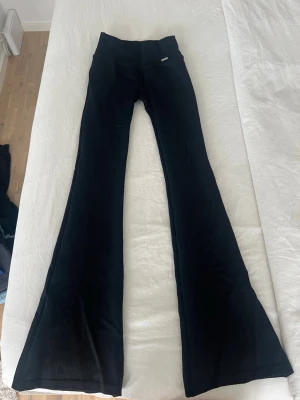 Svarta utsvängda leggings Aimn  - Säljer ett par svarta leggings med utsvängda ben och ribbad struktur. De har hög midja och en tight passform upptill som blir vidare nedtill. Perfekta för en trendig och avslappnad stil.