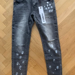 Grå slim jeans från Purple Brand - Grå jeans från Purple Brand med slim fit. Byxorna har slitna detaljer vid knäna och är dekorerade med vita färgstänk.