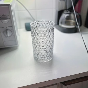 Genomskinlig mönstrad glasvas – fint skick - En genomskinlig vas i mönstrat glas, inköpt secondhand för cirka 300kr och endast använd vid ett tillfälle. Vasen är noggrant diskad. Mindre märken finns kvar på insidan som inte gick att få bort, men dessa påverkar inte helhetsintrycket nämnvärt. I övrigt är vasen i mycket fint skick. Passar utmärkt för blommor eller som en stilren dekorativ detalj i hemmet. FÖRST TILL KVARN! (SISTA BILDEN ÄR TAGEN MED MIN KAMERA!)