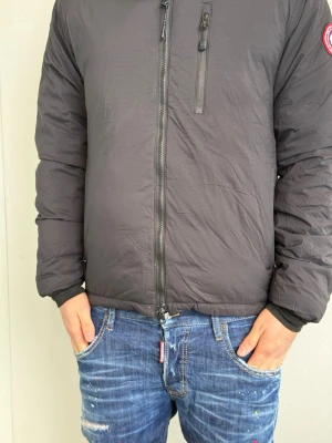 Svart dunjacka från Canada Goose - Säljer en svart dunjacka från Canada Goose med dragkedja framtill och en bröstficka med dragkedja. Jackan har det klassiska runda Canada Goose-märket på ärmen och är perfekt för kalla vinterdagar. Stilsäker och varm design som funkar till det mesta. Han bilden är 175cm och väger 74kg