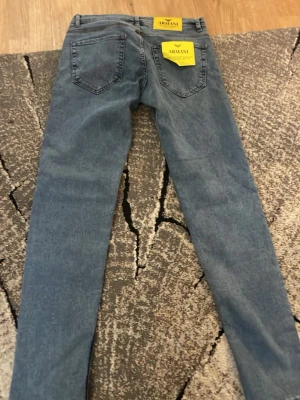 Blå slim fit jeans från Armani - Säljer ett par blå slim fit jeans från Armani med klassisk femficksdesign och normalhög midja. Jeansen har en snygg tvättad look och är tillverkade i mjukt denimtyg som ger en skön passform. Perfekta till en avslappnad streetstyle.