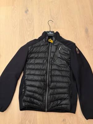Svart dunjacka från Parajumpers - Snygg svart dunjacka från Parajumpers med quiltad front och släta ärmar. Jackan har dragkedja framtill, bröstficka med dragkedja och klassisk gul detalj vid kragen. Perfekt för kyliga dagar och har en modern, sportig look. Den är precis hämtad från kemtvätt ren och fräsh!  Storlek medium