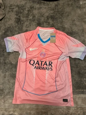 PSG rosa matchtröja Nike - Säljer en snygg PSG matchtröja i rosa och ljuslila med blå detaljer. Tröjan har korta ärmar, rund halsringning med blå kant och Qatar Airways-logga på bröstet. Tillverkad i lätt och ventilerande material, perfekt för fotboll eller träning.