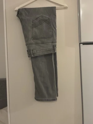 Grå raka jeans med kontrastsömmar - Säljer ett par grå jeans med raka ben och tydliga kontrastsömmar. Jeansen har klassiska fem fickor och en något tvättad look. Perfekta för en avslappnad stil och passar till det mesta. Materialet är denim i bomull.