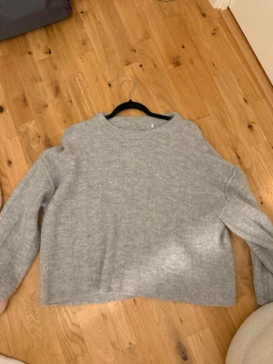 Ljusgrå stickad tröja i boxy modell - Mysig ljusgrå stickad tröja med rak, boxy passform och diskret ribbat mönster. Tröjan har rund halsringning och långa ärmar. Perfekt för lager-på-lager och chill dagar.