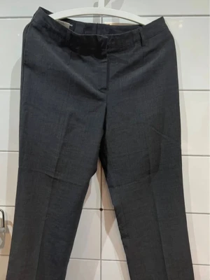 Mörkgrå kostymbyxor från Johan Skoglund - Snygga mörkgrå kostymbyxor från Johan Skoglund i klassisk rak modell. Byxorna har diskreta fickor och är tillverkade i ett slätt tyg som ger en stilren look. 