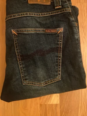 Nudie Jeans mörkblå denimjeans - Snygga mörkblå jeans från Nudie Jeans grim trim  31/32, har blivit lagade i skrevet hos nudie gjort snyggt skriv vid funderingar🔥🔥
